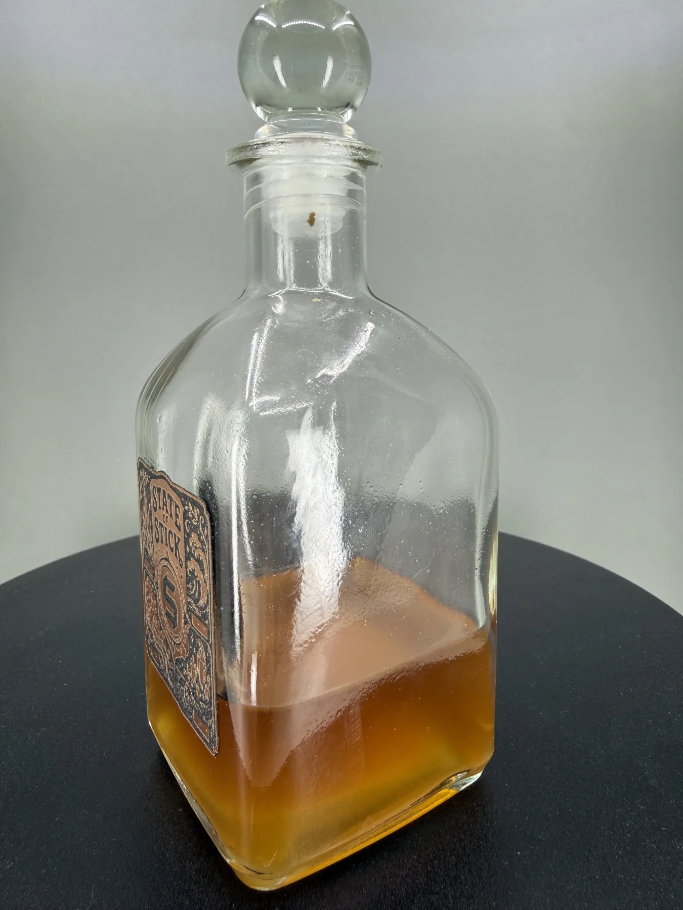 Angled view showing the dimensional emblem, glass bottle, and amber botanical resin preparation