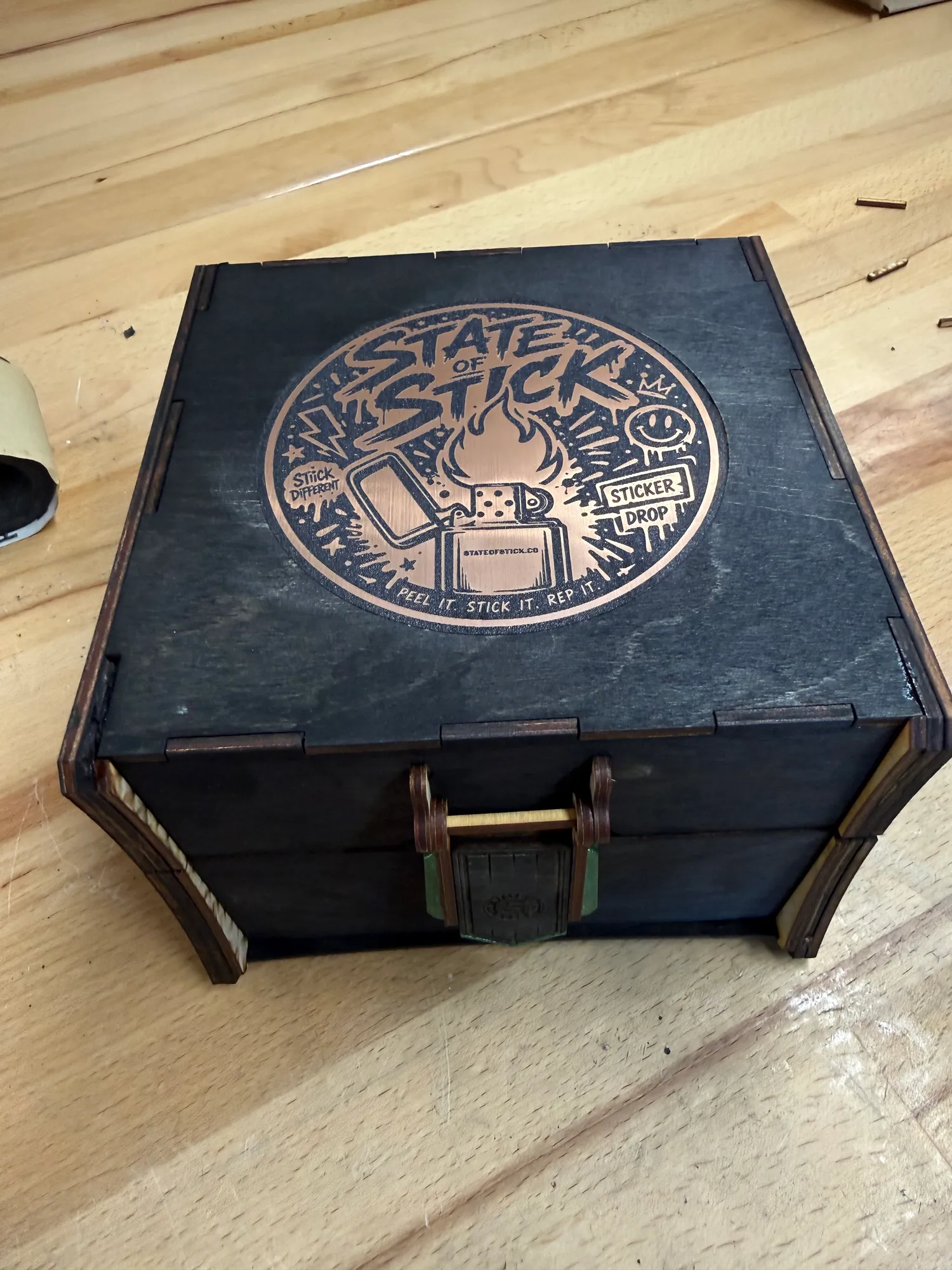 Closed black laser-cut display box with a copper State of Stick emblem and custom latch