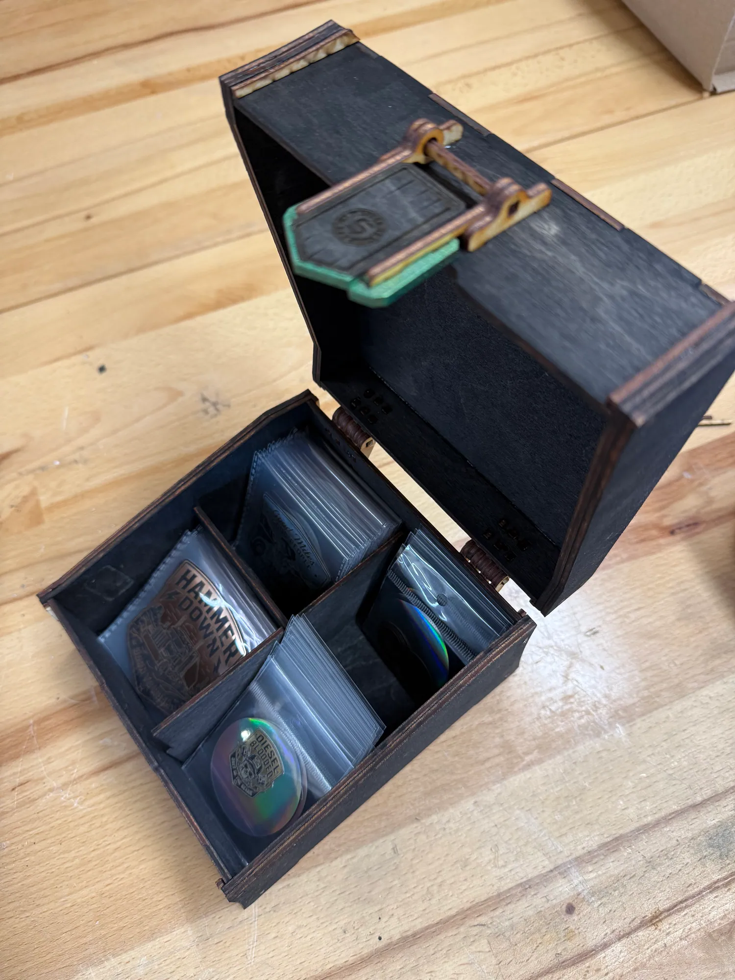 Open State of Stick laser-cut display box with divided compartments holding packaged emblems